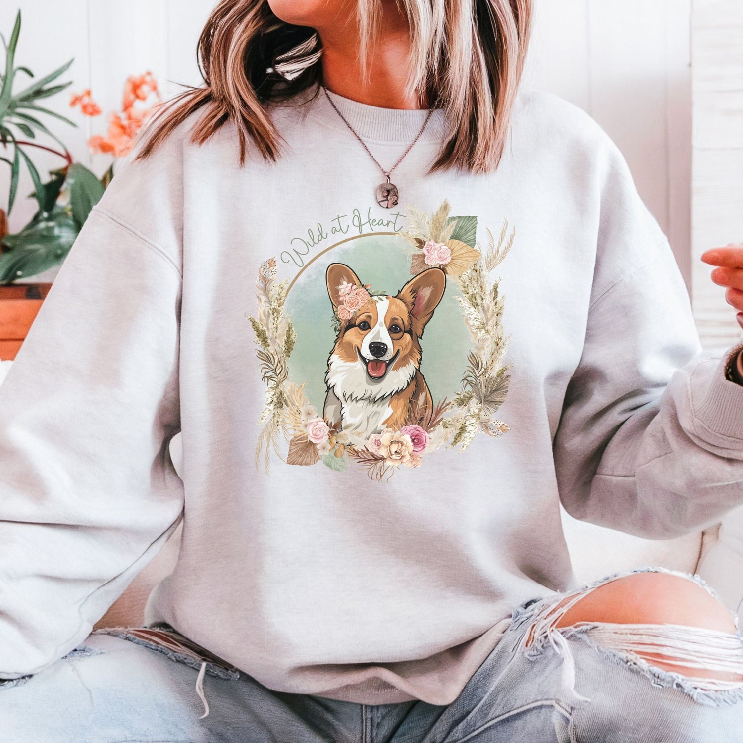 Crewneck Sweatshirt with a boho style featuring a corgi with flowers and a feathery border, including the text “Wild at Heart”